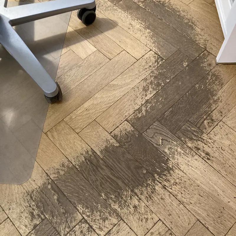 Lakattu parketti, josta työtuolin pyörät ovat kuluttaneet lakan harmaaksi kaareksi.